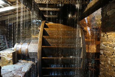 In einem von alten Natursteinmauern gefassten Becken dreht sich ein riesiges hölzernes Wasserrad, von oben tropft das Wasser in Strömen.