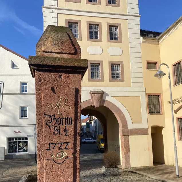 Vor einem historischen Gebäude mit der Aufschrift "Museum" steht eine alte Postmeilensäule aus rotem Porphyr.
