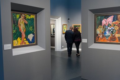 „Unmittelbar und unverfälscht“: Raumimpression Max-Pechstein-Museum In einem Ausstellungssaal mit großformatigen Gemälden in kräftigen Farben stehen zwei Personen, die in die Kunstbetrachtung vertieft sind.