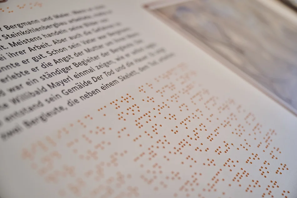Nahaufnahme einer taktilen Station, der sogenannten Kohleninsel, mit Text in Schwarzschrift und Brailleschrift