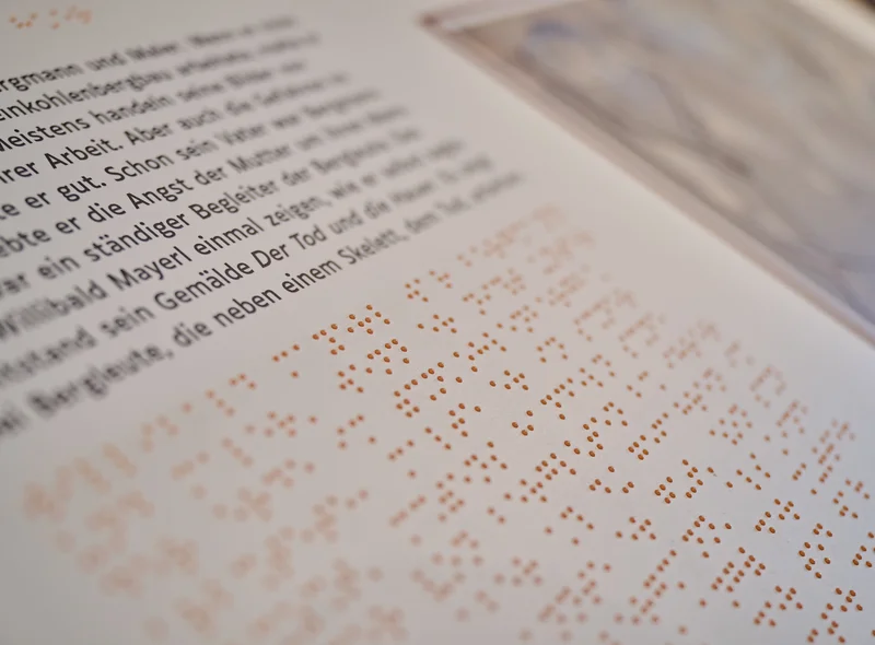 Nahaufnahme einer taktilen Station, der sogenannten Kohleninsel, mit Text in Schwarzschrift und Brailleschrift