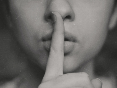 Auf dem Bild sieht man eine Frau, die ihren Zeigefinger auf ihrem Mund hat. Sie symbolisiert Stille.