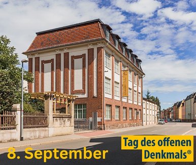 Tag des offen Denkmals 2024 in der Tuchfabrik Gebr. Pfau Crimmitschau An einer beidseitig von Häusern gesäumten Straße steht ein dreistöckiges Klinkergebäude mit Kassettenfenstern. Unten stehen die Worte "Tag des offenen Denkmals" und das Datum "8. September".