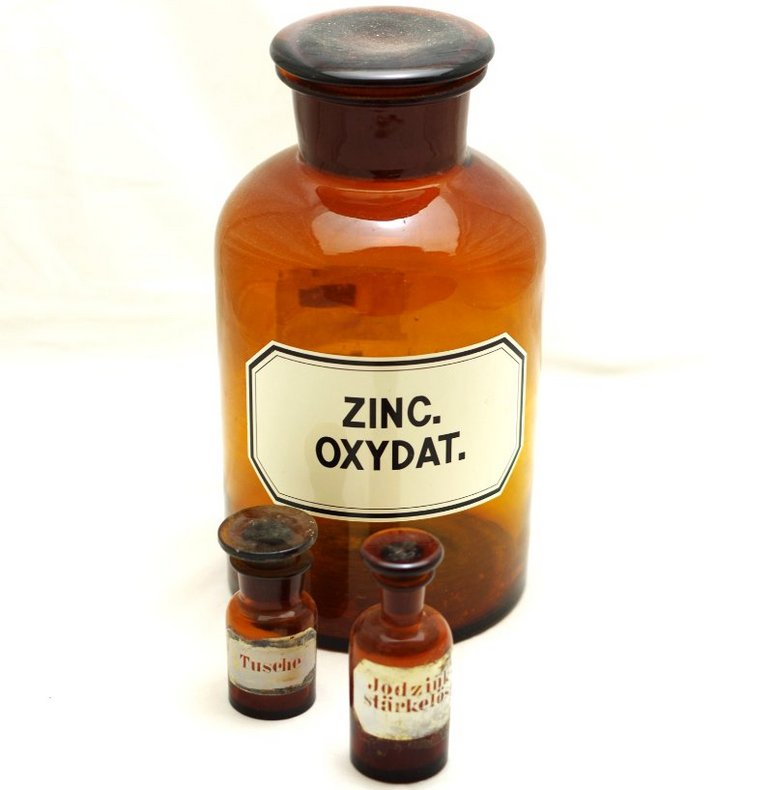 Drei historische Apotheker-Fläschchen aus braunem Glas, die größte ist etikettiert mit den Worten "Zinc Oxydat".