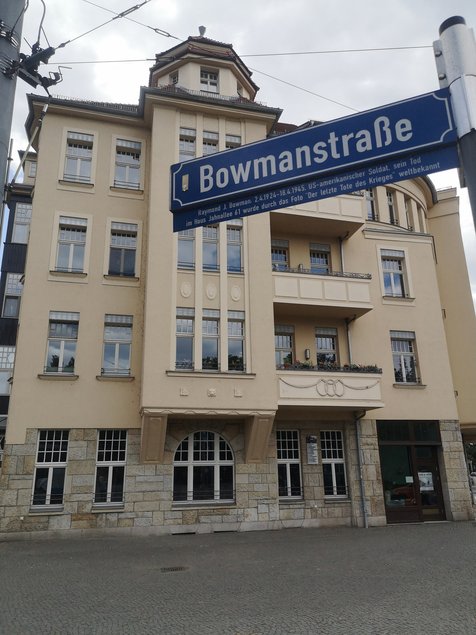 Ein vierstöckiges Gründerzeithaus mit gelber Fassade und Balkonen, im Vordergrund das Straßenschild Bowmannstraße