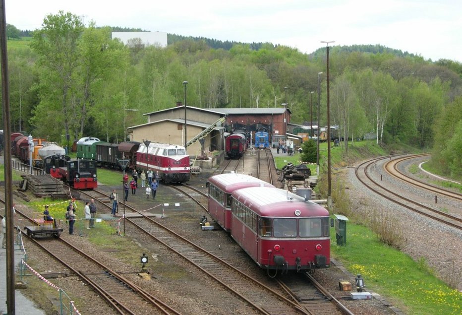 Im Vordergrund ein historischer Dieseltriebwagen, im Hintergrund mehrere historische Lokomotiven, Waggons und ein Lokschuppen
