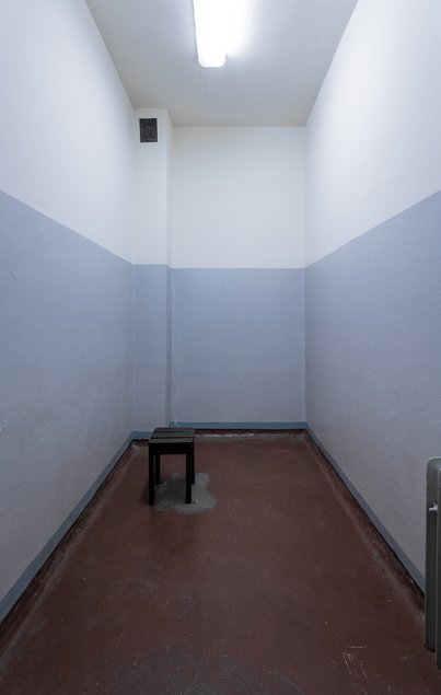 Das Foto zeigt eine nahezu leere, nur mit einem Holzhocker ausgestattete Arrestzelle in der ehemaligen der Bezirksverwaltung Dresden des DDR-Ministeriums für Staatssicherheit.
