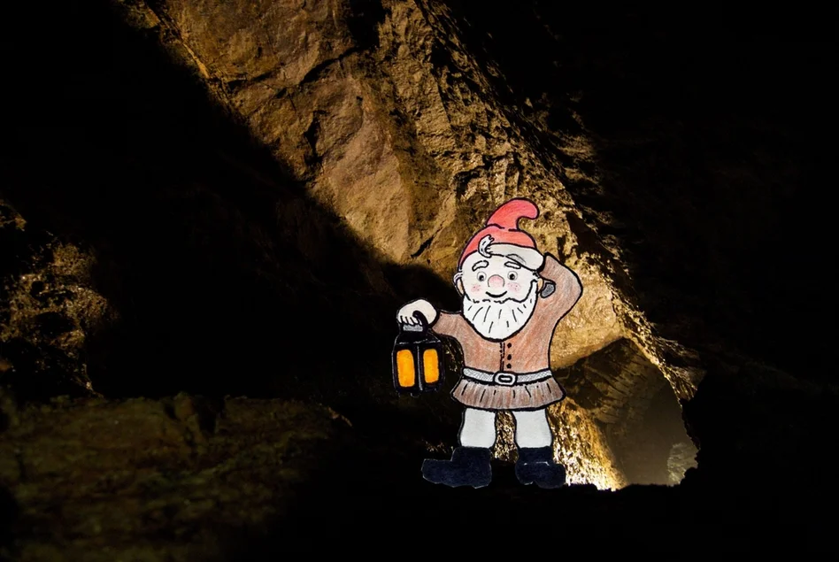 Im Reich des kleinen Bergzwergs Collage, in der die Zeichnung eines Wichtels mit roter Mütze und Laterne auf das Foto eines Bergbaustollens gesetzt wurde