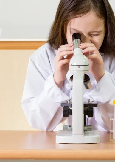 Kleines ganz groß Foto eines an einem Tisch sitzenden Kindes, das aufmerksam in ein Mikroskop schaut