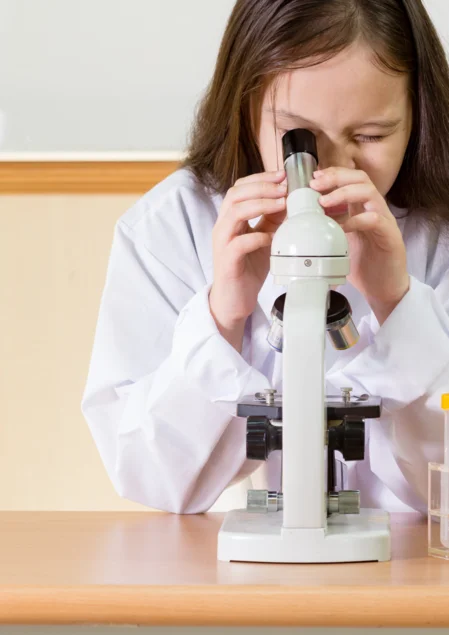 Kleines ganz groß Foto eines an einem Tisch sitzenden Kindes, das aufmerksam in ein Mikroskop schaut