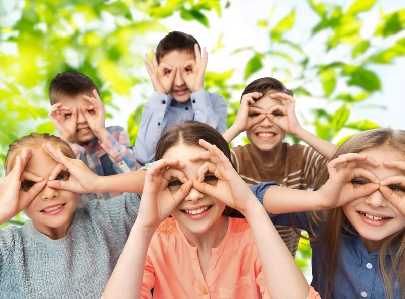 Kinder bilden mit den Händen Ferngläser vor ihren Augen und blicken uns an.