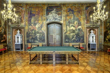 Ein prunkvoll ausgestatteter Saal mit einem Billiardtisch im Zentrum und reich verzierten Goldledertapeten im Hintergrund