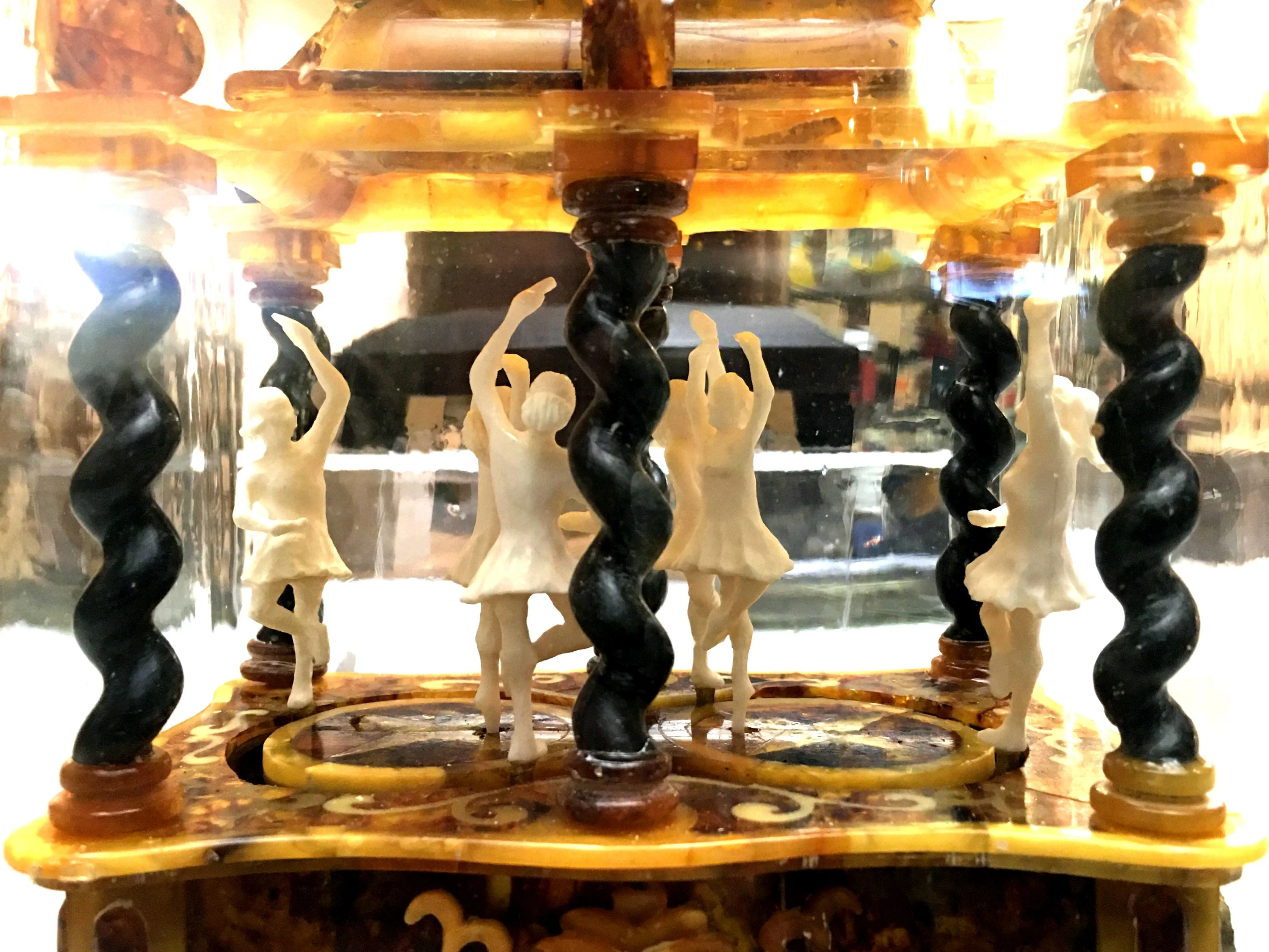 Zwischen schwarzen, spiralförmig gedrehten Säulen tanzen kleine, weiße Ballettfiguren.