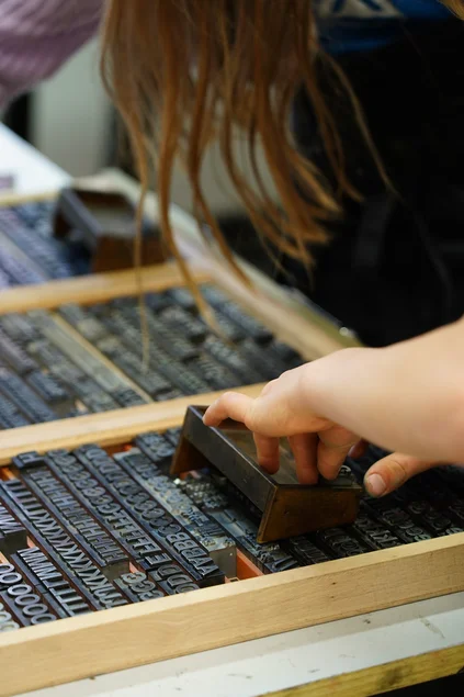 Nahaufnahme einer Kinderhand, die bewegliche Lettern aus einem Setzkasten entnimmt