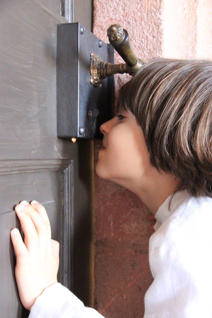 Ein Kind lugt durch das Schlüsselloch einer historischen Tür.