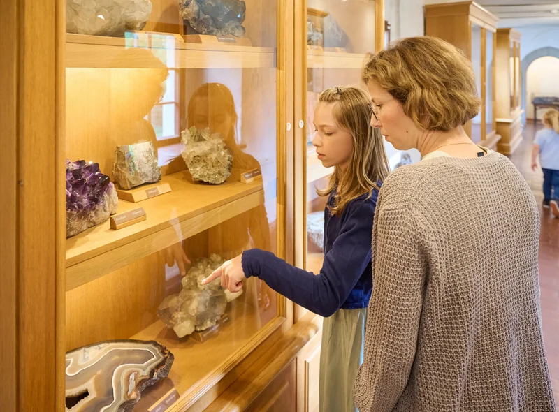 Ein Kind und eine erwachsene Person betrachten Minerale in einer Museumsvitrine.