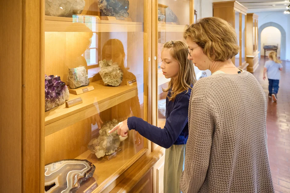 Ein Kind und eine erwachsene Person betrachten Minerale in einer Museumsvitrine.