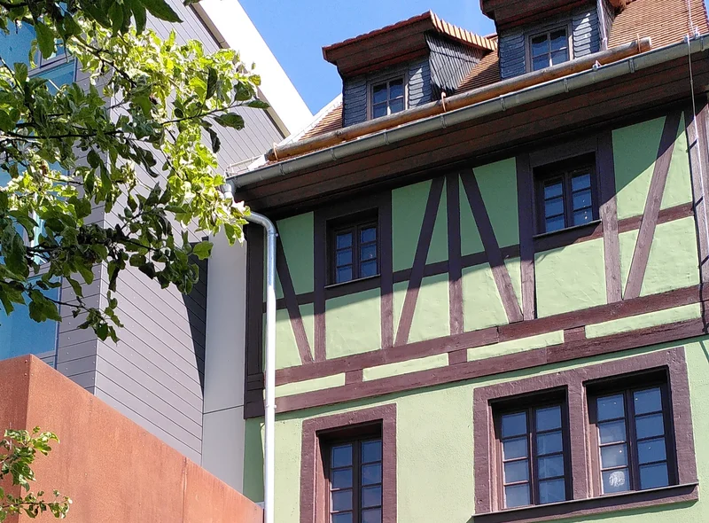 Ein grünes Fachwerkhaus neben einem modernen Neubau