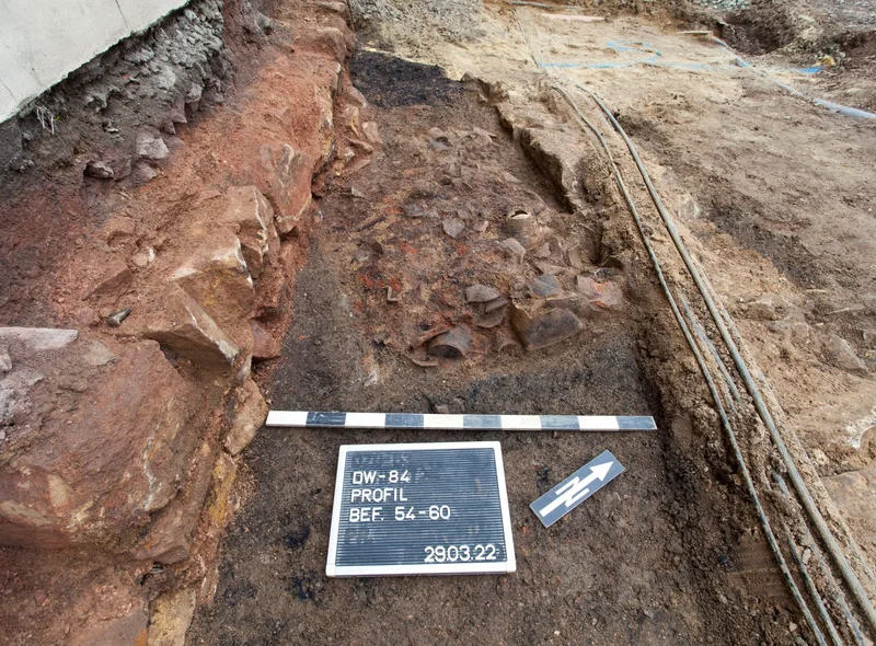 Ausschnitt einer archäologischen Grabungsstelle mit Zollstock, Kennzeichnung und Beschilderung