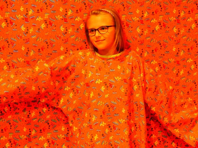 Tarnen in der Sonderausstellung „More than Colours“ Ein Kind steht vor einer Wand. Durch eine großflächige orangefarbene Projektion verschmilzt das Kind optisch mit der Wand.