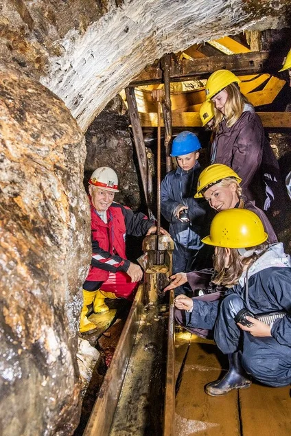 Die Ehrenfriedersdorfer Radpumpe Ein Bergwerksführer zeigt zwei Frauen und zwei Kindern eine hölzerne Rinne vor der Radpumpe im Besucherbergwerk.
