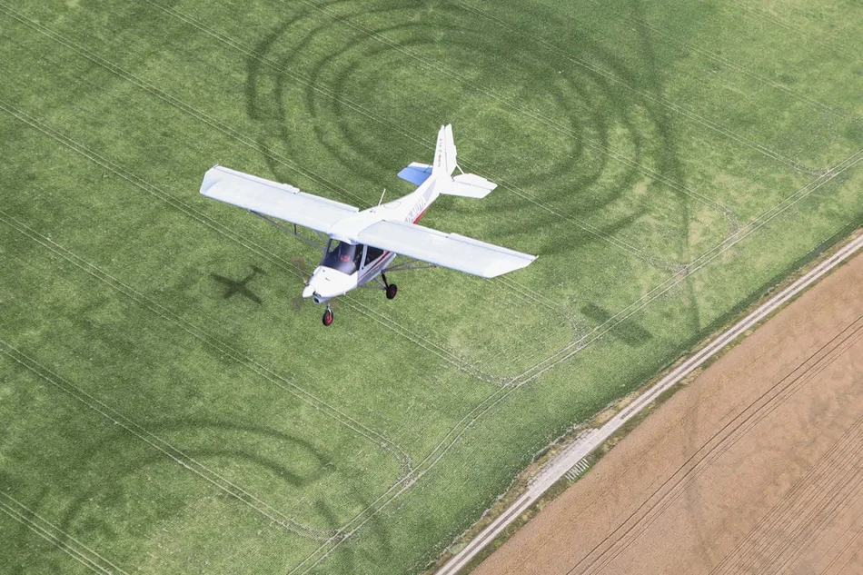Plakatmotiv ist eine Fotomontage mit einem über eine Landschaft mit Spuren archäologischer Funde fliegenden Leichtflugzeug