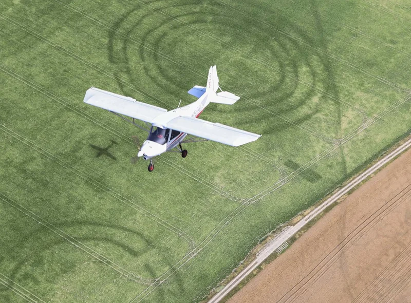 Plakatmotiv ist eine Fotomontage mit einem über eine Landschaft mit Spuren archäologischer Funde fliegenden Leichtflugzeug