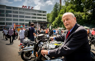 Prof. Dr. Carl Horst Hahn in Zschopau 2021 Ein älterer Herr in Anzug steht an einem Motorrad der Marke MZ vor dem MZZ-Fabrikgebäude, im Hintergrund viele Motorradfahrer