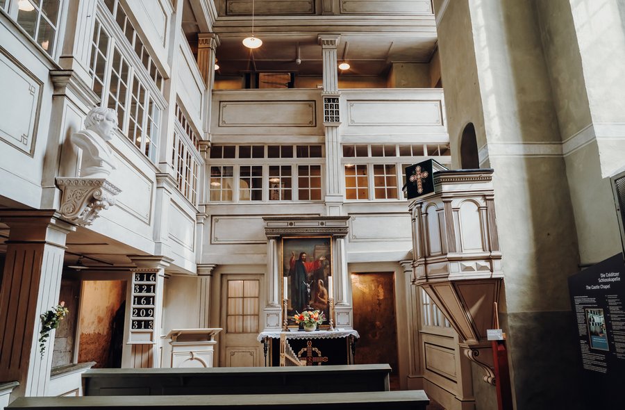 Blick ins Innere einer schnörkellosen Kapelle mit weißen Wandvertäfelungen und drei Emporen. Einziger farbiger Blickfang ist das Altargemälde.