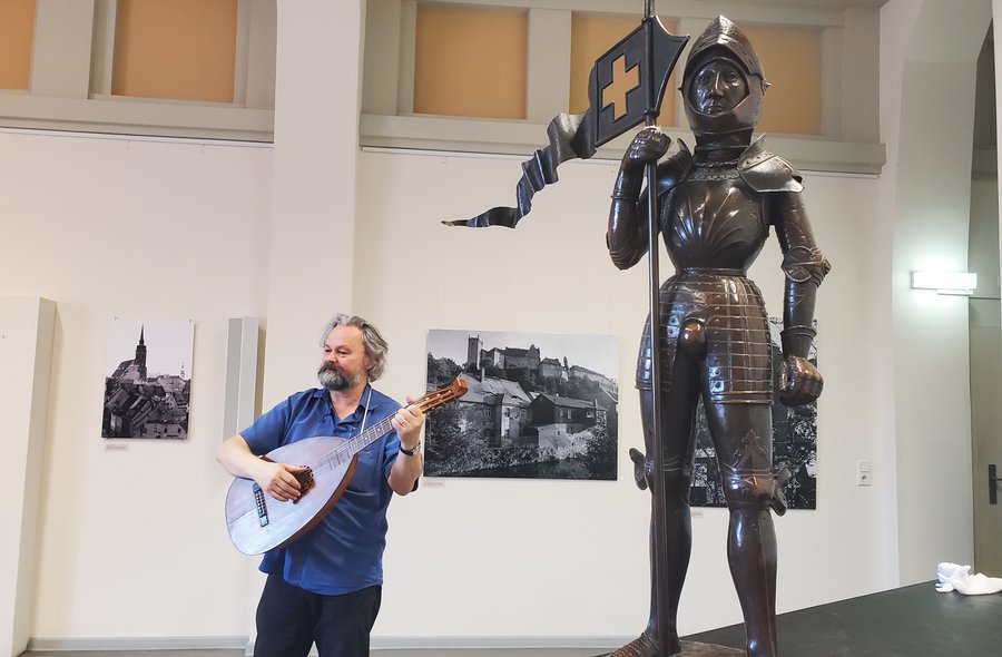 In einen Museumsraum steht auf er linken Seite das Modell eines Ritters, während auf der rechten Seite ein Mann eine Laute spielt.