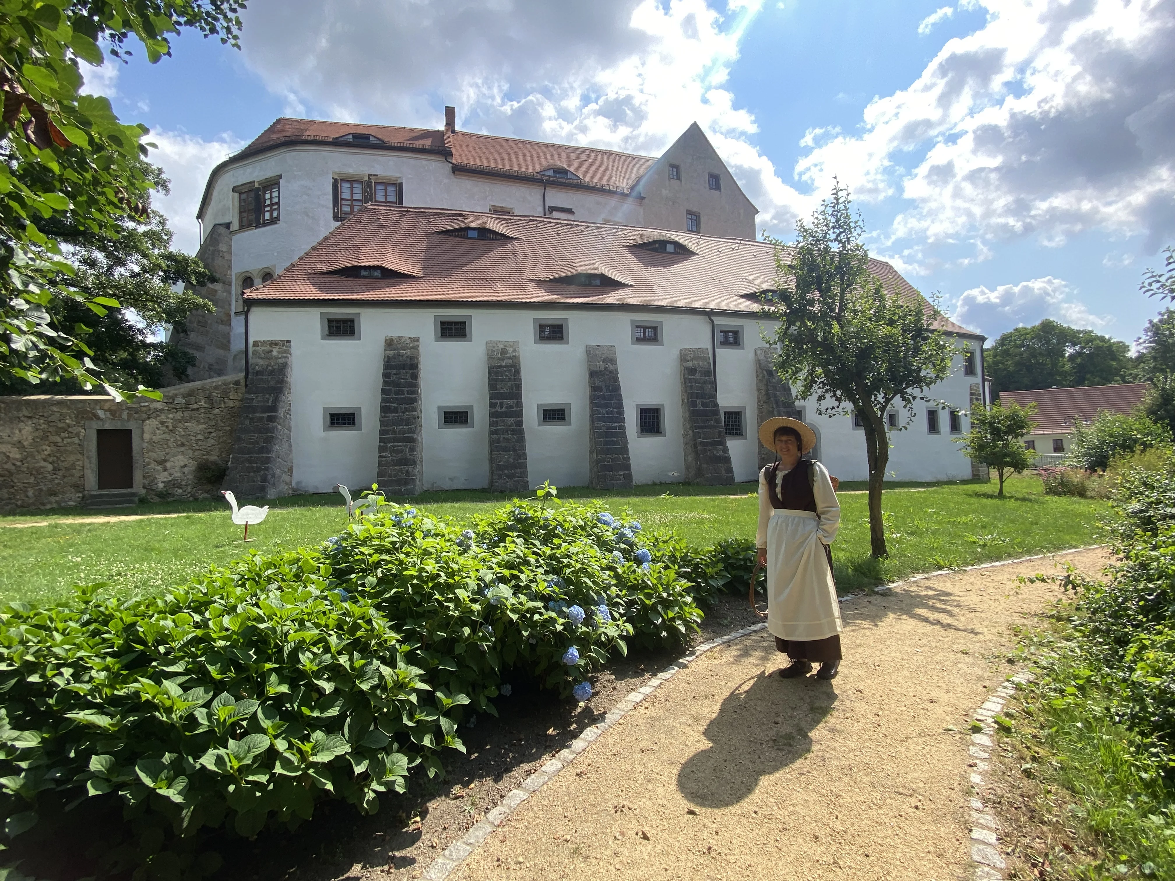 Eine Magd vor Schloss Klippenstein Als Magd verkleidete Person steht im Garten vor den Toren des weiß getünchten Schlosses.