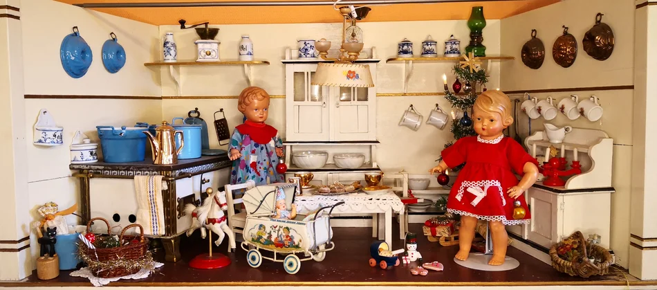 Zwei Püppchen stehen in einer detailverliebt ausgestatteten historischen Puppenküche.