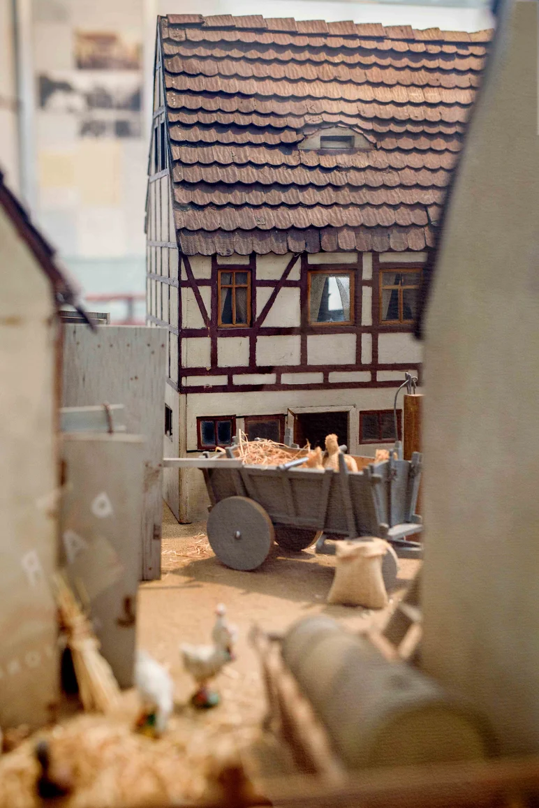 Blick durch eine Gasse auf ein Fachwerkhaus; auf dem Hof steht ein mit Heu gefüllter Karren.
