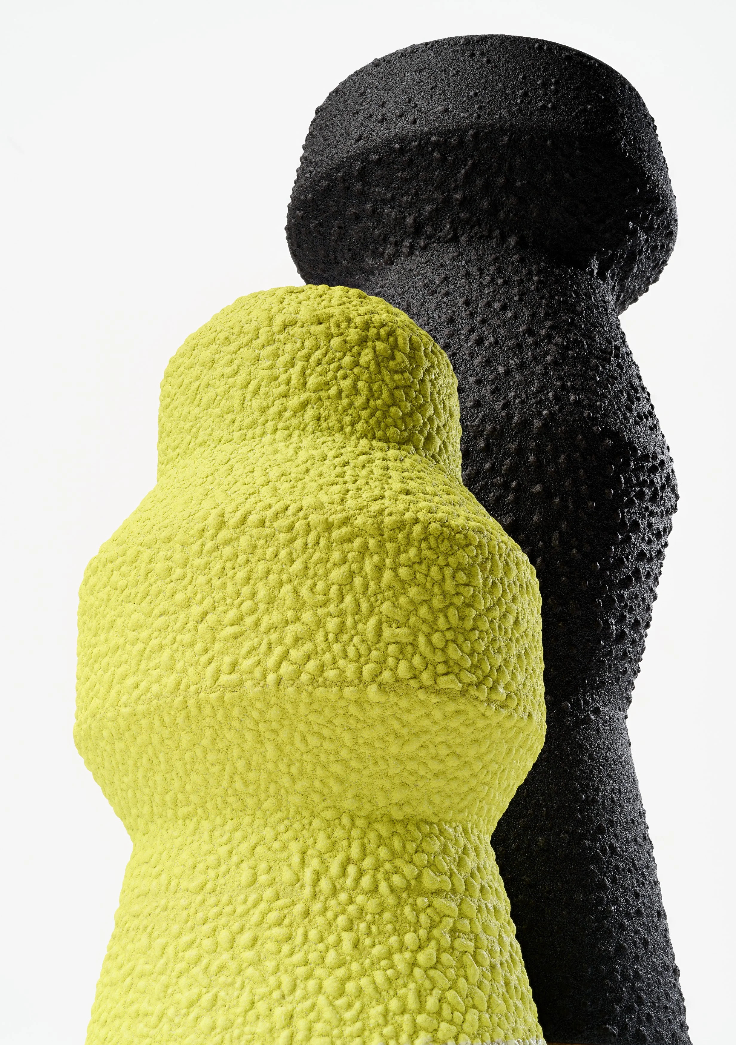 Zwei Vasen stehen versetzt hintereinander, die vordere hat eine neongelb, die hintere eine schwarze Glasur.