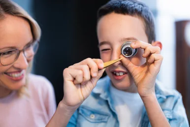 Ein Junge schaut sich ein winzig kleines Uhrenteil durch eine Uhrmacherlupe an.