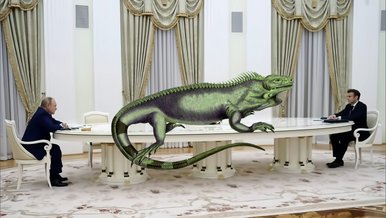 Videostill Ein riesiger ovaler Tisch steht in einem großen, mit opulenten Gardinen versehenen Raum. Am linken Tischende sitzt Wladimir Putin, am weit entfernten gegenüberliegenden Ende ein anderer Politiker. Collagen-artig nimmt eine riesige grüne Echse die Länge des Tisches ein.