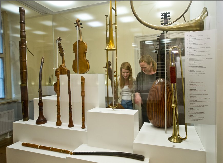 Das Foto zeigt zwei Besucherinnen des Bach-Museums Leipzig, die mehrere in Vitrinen ausgestellte historische Musikinstrumente betrachten.