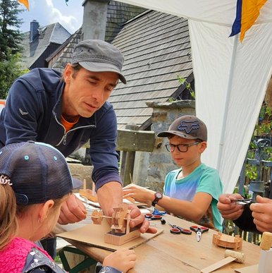 UNESCO-Welterbetag im Frohnauer Hammer An einem im Freien stehenden Tisch hilft ein Erwachsener zwei Kindern beim Basteln von Miniatur-Wasserrädern.