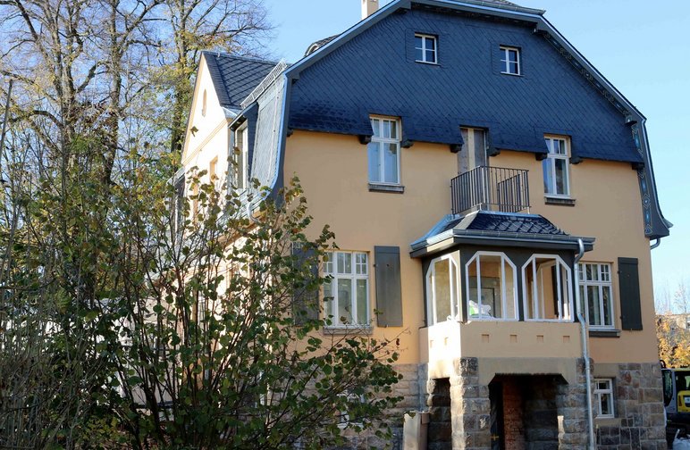 Zweistöckige Villa mit gelber Fassade, Erker, Balkon und dunklem Schieferdach