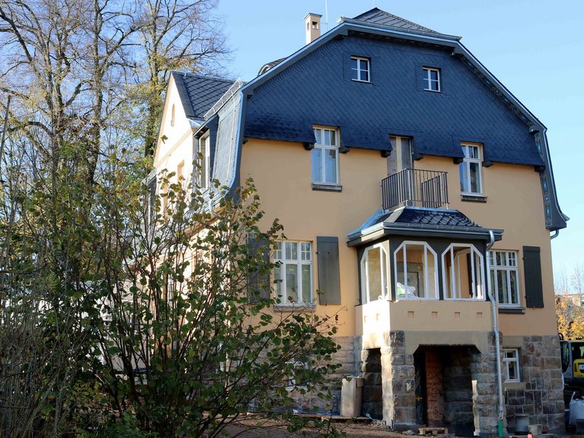 Zweistöckige Villa mit gelber Fassade, Erker, Balkon und dunklem Schieferdach