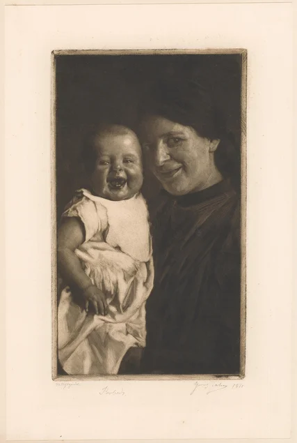 Eine lächelnde Mutter hält ein herzlich lachendes Kind auf dem Arm. Beide schauen den Betrachter direkt an.