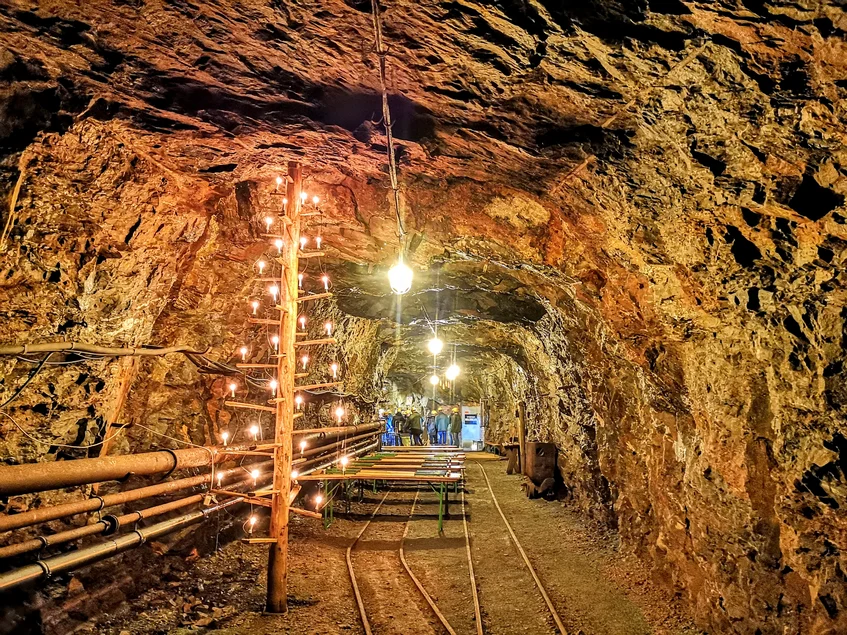 Mehrere Tische in einem Stollen, der mit Deckenlichtern und einem schlichten Weihnachtsbaum aus Holz beleuchtet wird. Im Hintergrund sind einige Personen mit Schutzhelmen zu sehen.