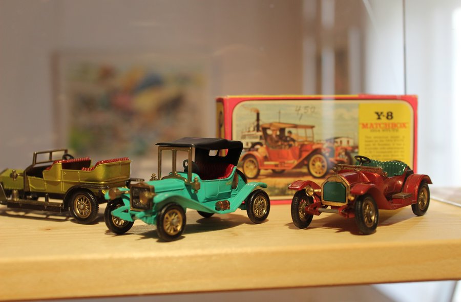 Nahaufnahme von drei Matchbox-Autos in Form dreier Oldtimer, im Hintergrund eine historische Matchbox-Schachtel