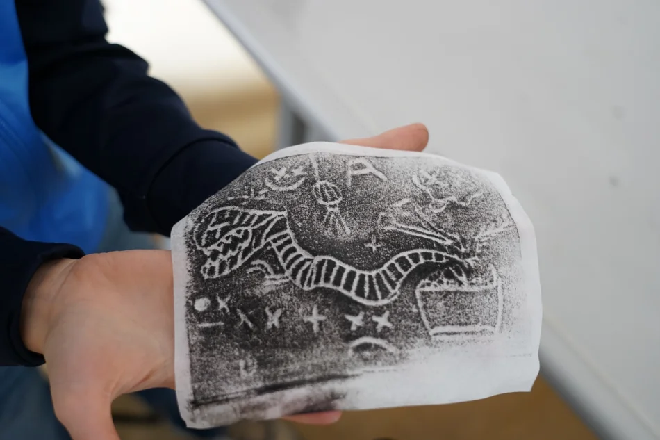 Zwei Hände halten ein Papier, auf das mit schwarzer Farbe ein abstraktes Motiv gedruckt ist.