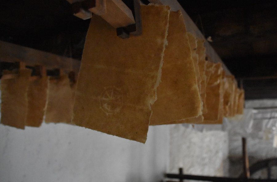 Trocknendes Büttenpapier Das Foto zeigt eine große Zahl frisch geschöpfter Blatt Büttenpapier, die zum Trocknen von einer Holzbalkendecke hängen.