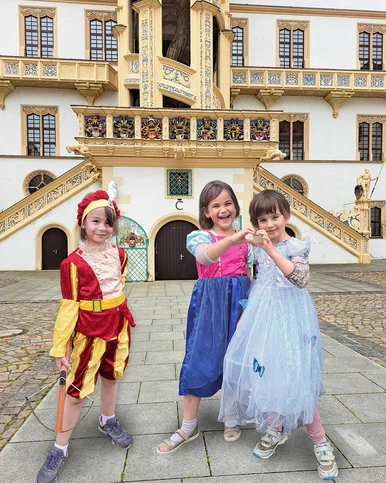 Drei Mädchen in Renaissance-Kleidern posieren vor dem Großen Wendelstein von Schloss Hartenfels in Torgau.