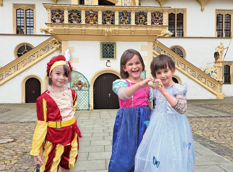 Drei Mädchen in Renaissance-Kleidern posieren vor dem Großen Wendelstein von Schloss Hartenfels in Torgau.