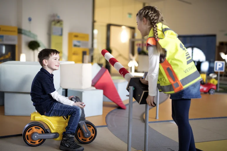 Junge auf Bobbycar und Mädchen an Schranke im Verkehrsgarten