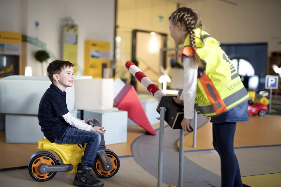 Junge auf Bobbycar und Mädchen an Schranke im Verkehrsgarten