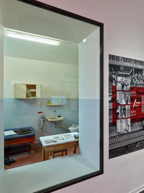 Das Foto zeigt ein Schaufenster. Hinter der Glasscheibe ist eine Gefängniszelle zu sehen mit einem schmalen Tisch mit Hocker und der SED-Zeitung "Neues Deutschland", einem kleinen Hängeschrank an der Wand und einer kargen Holzpritsche mit einer Matratze.